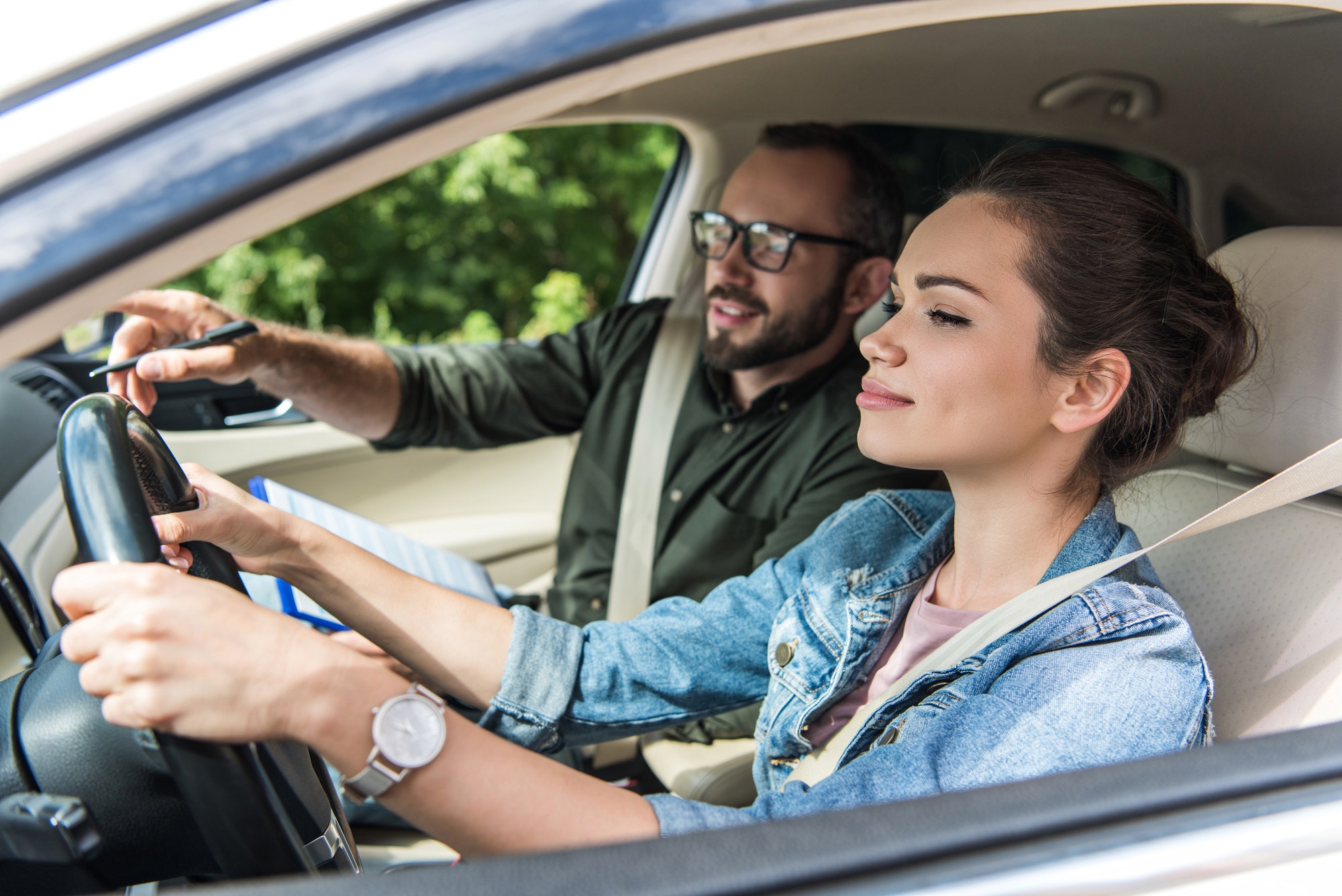 cheerful student and teacher in car at driving test